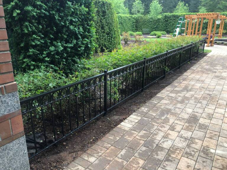 Black ornamental metal fence along a paver walkway