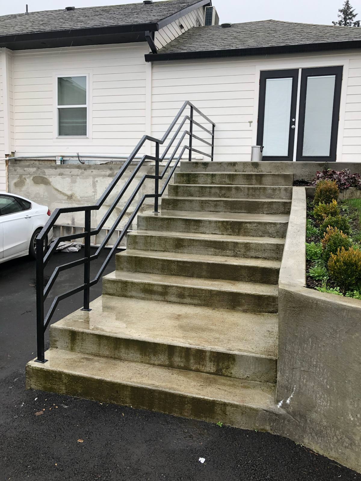 Black metal handrail on concrete front steps by Cascade Mobile Welding