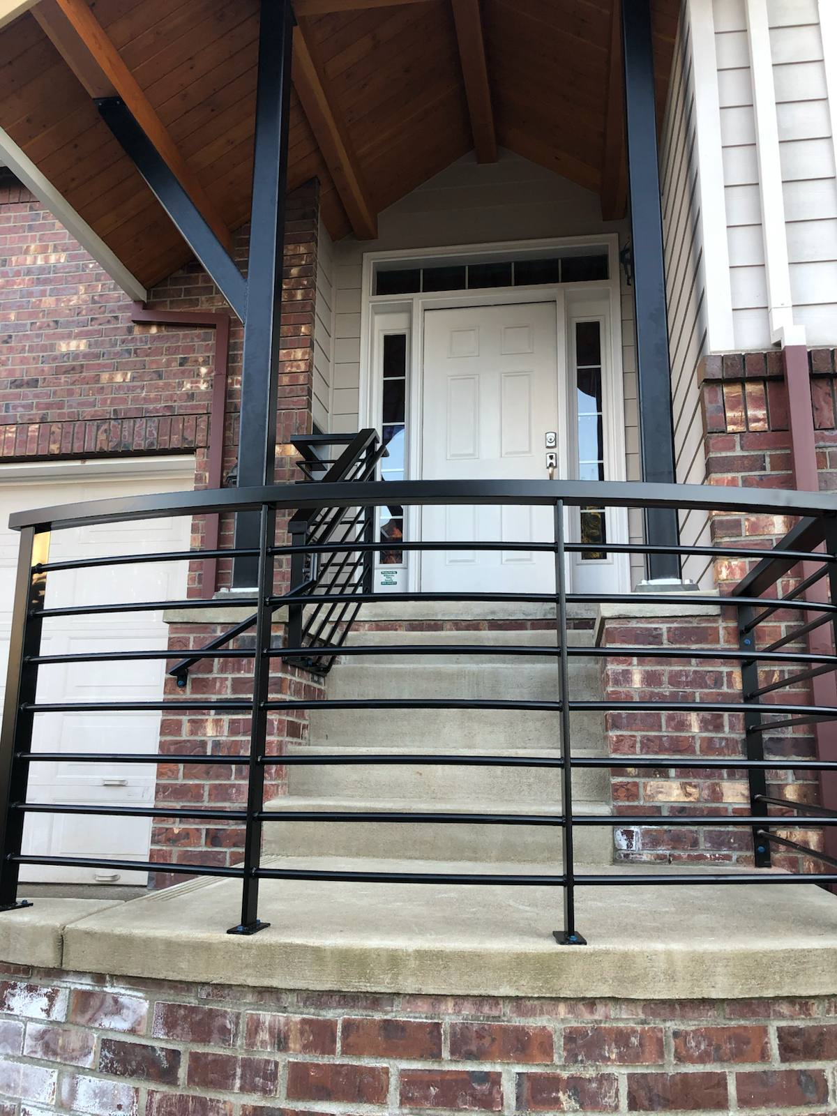 Black metal handrail on concrete front steps by Cascade Mobile Welding