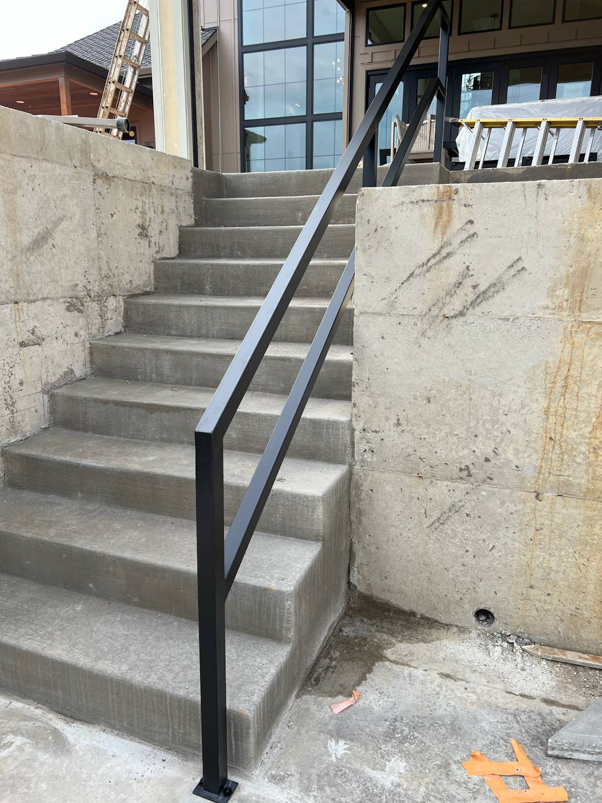 Black metal handrail on concrete front steps by Cascade Mobile Welding